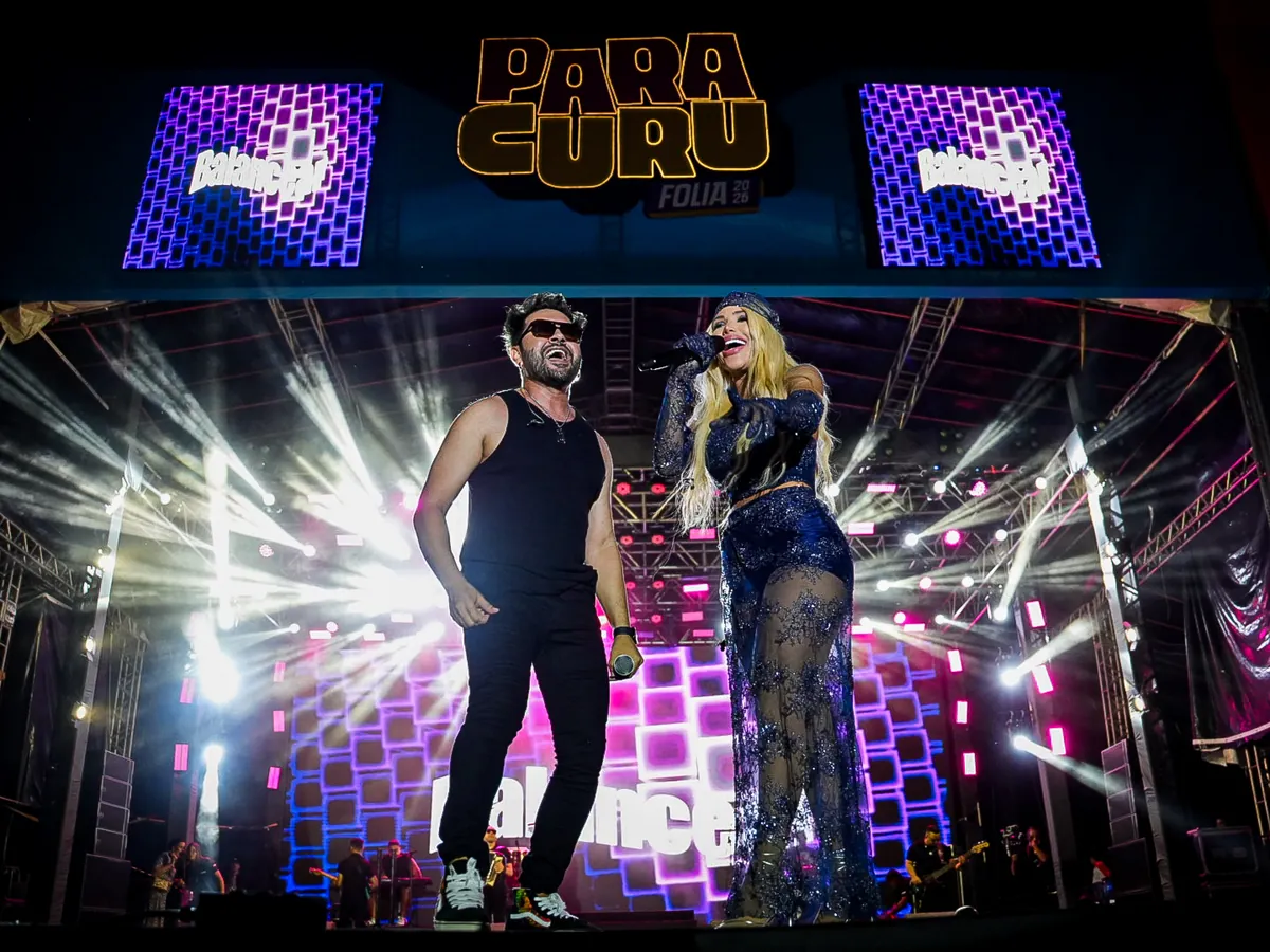 Léo Lira e Jack Lins cantam lado a lado no palco do Paracuru Folia 2026, sob o painel do evento e feixes de luz.
